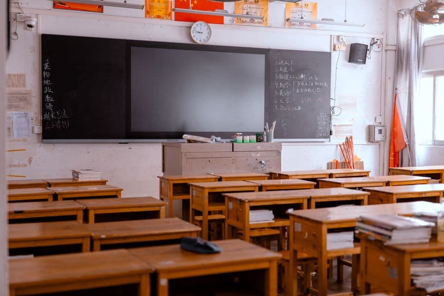 An empty classroom with wooden desks and a blackboard, featuring educational materials.